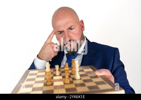 ritratto dell'uomo d'affari in tuta blu e cravatta con un'espressione premurosa che guarda la scacchiera isolata su sfondo bianco Foto Stock