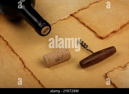 Primo piano una bottiglia di vino rosso completamente aperta con tappo e apriporta retrò con manico in legno su fondo di carta marrone vintage con spazio copia, alto Foto Stock