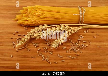 Mazzo legato di spaghetti secchi adagiati su un tagliere di legno vicino alle orecchie di frumento e grani, che rappresentano la cucina tradizionale italiana e una sana alimentazione, Foto Stock