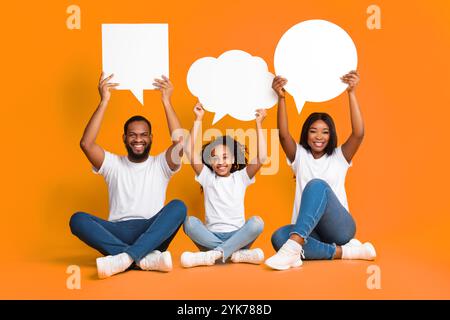 Sorridente famiglia nera che si accoviglia bolle di parole in studio Foto Stock