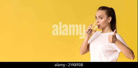 Bella giovane donna che beve acqua minerale e mostra il gesto del pollice Foto Stock