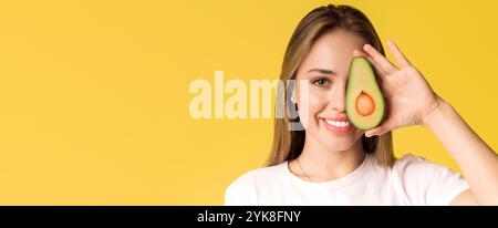 Felice giovane donna che tiene avocado mezzo, coprente l'occhio con frutta sana Foto Stock