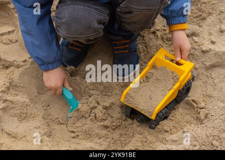 Bambini che giocano in una scatola di sabbia con un camion giocattolo e una pala di plastica. Attività all'aperto, creatività infantile e gioco creativo in ambiente naturale Foto Stock