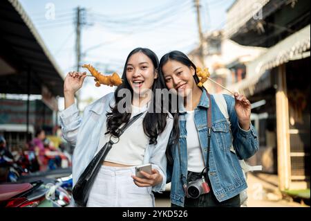 Un ritratto di due bellissime e gioiose giovani turisti asiatici si godono il cibo di strada in Thailandia mentre esplorano la città. Sud-est asiatico, vacanze, Foto Stock