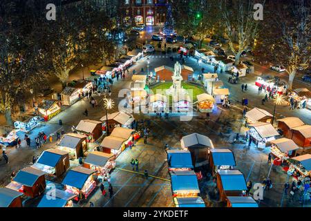 Vista aerea di un tradizionale e vivace mercato di Natale in una piazza italiana con bancarelle di legno, luci festose e decorazioni in serata. Foto Stock
