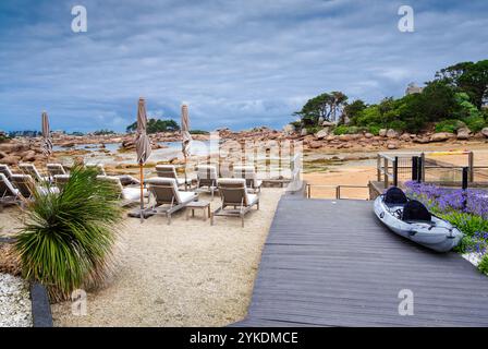 Una tranquilla spiaggia di Ploumanach, Bretagna, con sedie a sdraio disposte in modo ordinato su un'area sabbiosa, con un passaggio pedonale in legno che conduce alla riva Foto Stock