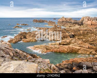 Un paesaggio costiero panoramico di Plougrescant, Bretagna, formazioni rocciose e acque limpide. Il cielo si sovrappone e le onde si infrangono delicatamente contro il rugg Foto Stock