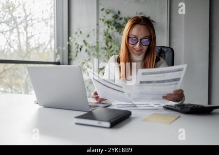 Donna d'affari sorridente che esamina documenti in Modern Office Foto Stock