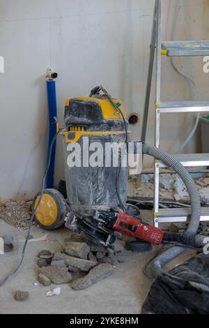 Un cantiere con un aspirapolvere industriale e una smerigliatrice angolare rossa circondata da detriti. Foto Stock