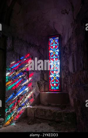 Una finestra di vetro colorato con il sole che splende creando ombre colorate su un muro di pietra Foto Stock