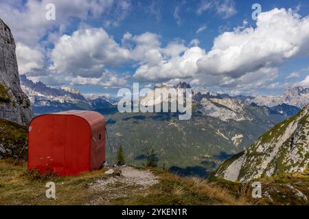 Rifugio alpino bivaco situato in un aspro terreno alpino. Rifugio rosso bivacco nelle Dolomiti. Struttura compatta contro paesaggi mozzafiato Foto Stock
