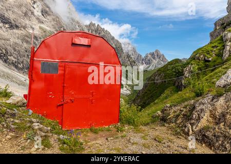 Rifugio alpino bivaco situato in un aspro terreno alpino. Rifugio rosso bivacco nelle Dolomiti. Struttura compatta contro paesaggi mozzafiato Foto Stock