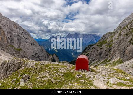 Rifugio alpino bivaco situato in un aspro terreno alpino. Rifugio rosso bivacco nelle Dolomiti. Struttura compatta contro paesaggi mozzafiato Foto Stock