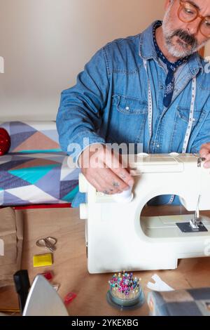 Un uomo che cucisce a casa con macchine da cucire Foto Stock