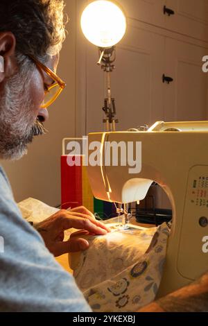 Un uomo che cucisce a casa con macchine da cucire Foto Stock