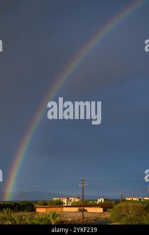 Uno splendido arcobaleno si estende attraverso il cielo, illuminando il tranquillo paesaggio del villaggio dopo un temporale. Foto Stock