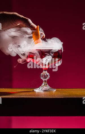 Un cocktail Negroni in un elegante vetro di cristallo, impreziosito da una decorazione agrumata, l'effetto fumato aggiunge un'aria di mistero ed eleganza, perfetta per un Foto Stock