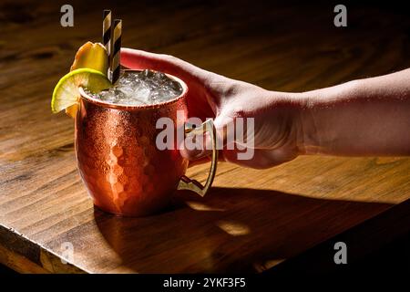 Un Moscow Mule servito in una classica tazza di rame, guarnita con lime e menta, appoggiato su un rustico tavolo in legno, perfetto per gli amanti dei cocktail e il bar- Foto Stock