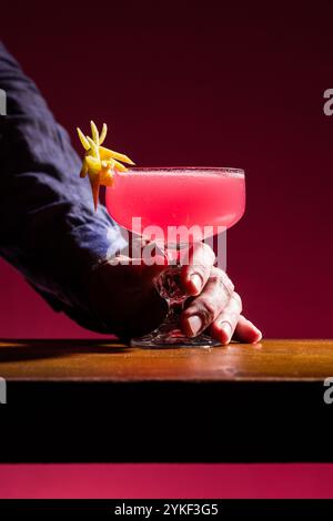 Il cocktail cosmopolita è presentato elegantemente in un bicchiere da coupé, adornato con un tocco di limone, la bevanda rosa contrasta splendidamente con il dorso Foto Stock