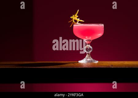 Il cocktail cosmopolita e' elegantemente presentato su una superficie di legno su uno sfondo scuro, la vivace bevanda rosa e' decorata con un tocco di agrumi, crea Foto Stock