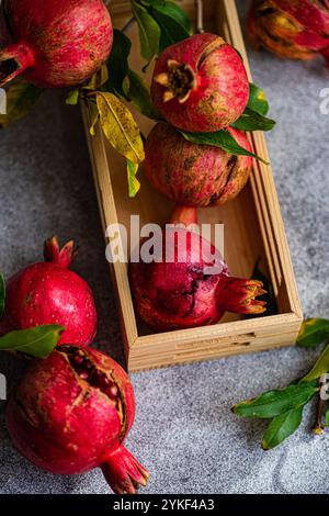 Dall'alto, questa immagine cattura vibranti melograni maturi posizionati in una cassa di legno. I frutti sono circondati da foglie fresche, aggiungendo un tocco di n Foto Stock