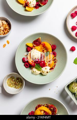 Piatti da dessert ben disposti con pesche a fette e palline di gelato alla vaniglia, guarniti con lamponi, fichi e una spolverata di tritatutto Foto Stock