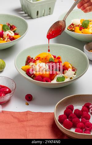 Una deliziosa ciotola da colazione con pesche a fette e gelato alla vaniglia condita con lamponi freschi e un vivace gocciolatoio di frutti di bosco Foto Stock
