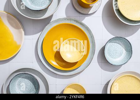 Vista dall'alto di una serie di ciotole e piatti in ceramica disposti artisticamente su piastrelle bianche. L'immagine mostra un assortimento di colori e texture, in alto Foto Stock