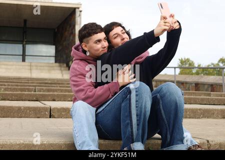 Una coppia LGBTQIA+ ama godersi un momento tenero all'aperto mentre si fa un selfie, con un uomo transgender in un ambiente informale che rappresenta l'orgoglio Foto Stock