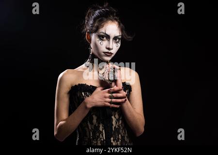 Una donna gotica vestita con un corsetto in pizzo nero si staglia su uno sfondo scuro il suo incredibile trucco, i suoi eleganti gioielli e l'orologio da tasca sottolineano un myst Foto Stock