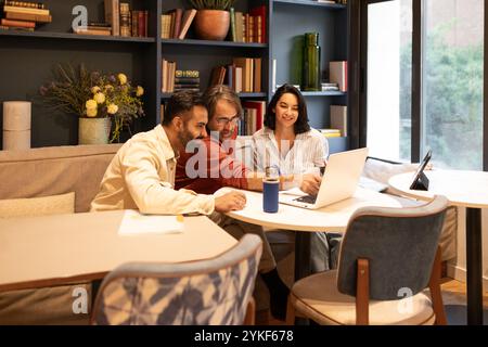 Un gruppo eterogeneo di professionisti collabora con entusiasmo in un moderno spazio di coworking, circondato da libri e piante, sottolineando la creatività e. Foto Stock