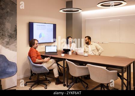 Un gruppo eterogeneo di professionisti si riunisce in un moderno spazio di coworking e si impegna a discutere e lavorare in modo collaborativo, utilizzando computer portatili e documenti Foto Stock