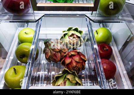 Un frigorifero ben organizzato con un'ampia scelta di frutta fresca. Sono visibili le mele verdi, le mele rosse mature e le vivaci strisce viola Foto Stock