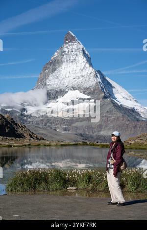 Una turista femminile si trova accanto a un tranquillo lago di montagna, con l'iconica vetta del Cervino sullo sfondo, che mostra la splendida bellezza naturale di Zermat Foto Stock