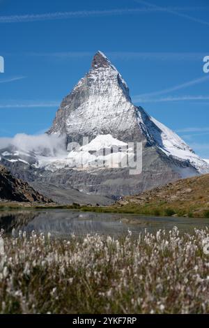 Immagini mozzafiato che catturano l'iconica vetta del Cervino a Zermatt, Svizzera, riflessa in un tranquillo lago di montagna, circondato da fiori selvatici sotto un cl Foto Stock