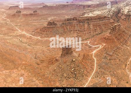 Dall'alto, questa immagine scattata con un drone mostra una strada sterrata tortuosa che si snoda attraverso l'aspro e arido paesaggio del deserto dello Utah. Il rosso roccioso tu Foto Stock