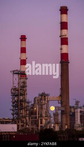 Dietro la sagoma dei camini industriali al crepuscolo a Porto sorge la suggestiva luna piena, catturando l'interazione tra natura e industria. Foto Stock