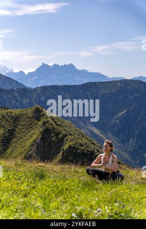 Una serena sessione di yoga si svolge nei prati lussureggianti di Rochers de Naye, sullo sfondo mozzafiato delle Alpi svizzere Foto Stock