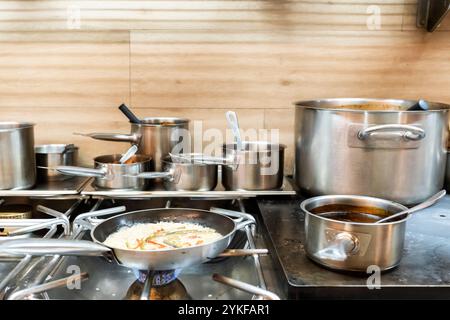 Una vivace cucina del ristorante cattura varie pentole e padelle utilizzate attivamente su una stufa. Questa immagine riflette un ambiente culinario professionale Foto Stock