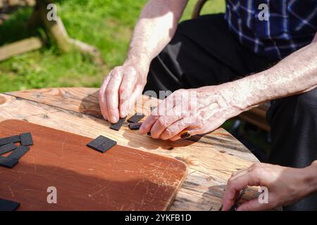 Primo piano irriconoscibile di un anziano uomo e donna caucasico che gioca a domino su un rustico tavolo di legno all'aperto, concentrandosi sulle mani e sul gioco p Foto Stock