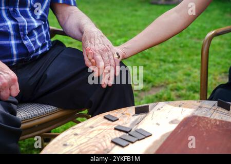 Uomo caucasico anziano cortato e irriconoscibile che tiene per mano una giovane donna vicino a un tavolo all'aperto, mostrando una stretta connessione durante un gioco da tavolo Foto Stock