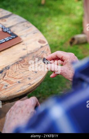 Uomo anziano corto e irriconoscibile che tiene in mano un pezzo di domino, concentrandosi sulle mani su un tavolo di legno all'esterno, catturando un momento tranquillo di svago. Foto Stock