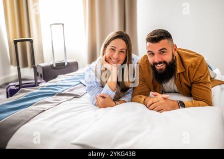 La giovane coppia felice è in vacanza. I turisti sono arrivati in camera d'albergo e si sono rilassati sul letto. Foto Stock