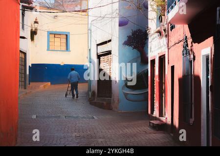 Guanajuato, Messico - 6 febbraio 2024: Un addetto alle consegne cammina attraverso un colorato vicolo acciottolato nel quartiere storico di Guanajuato, passando per Vibran Foto Stock