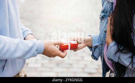 Primo piano della mano di un giovane che dà una piccola scatola rossa alla sua ragazza per San Valentino. Foto Stock