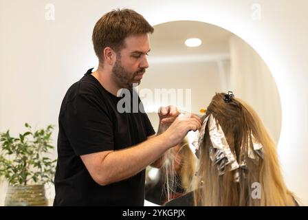 Friseur macht Foliensträhnen bei einer jungen Frau. Il parrucchiere strizza i capelli di una giovane donna Foto Stock