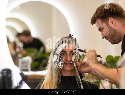 Friseur macht Foliensträhnen bei einer jungen Frau. Il parrucchiere strizza i capelli di una giovane donna Foto Stock