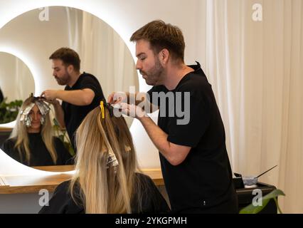 Friseur macht Foliensträhnen bei einer jungen Frau. Il parrucchiere strizza i capelli di una giovane donna Foto Stock