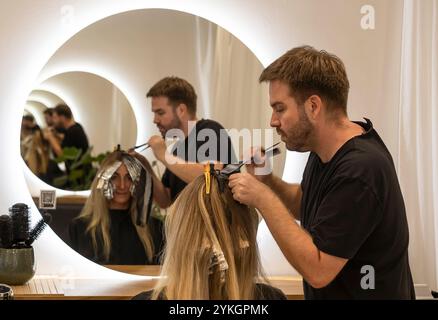 Friseur macht Foliensträhnen bei einer jungen Frau. Il parrucchiere strizza i capelli di una giovane donna Foto Stock