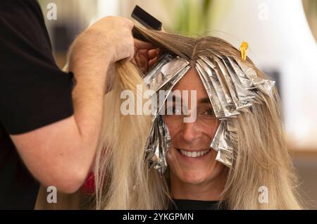 Friseur macht Foliensträhnen bei einer jungen Frau. Il parrucchiere strizza i capelli di una giovane donna Foto Stock